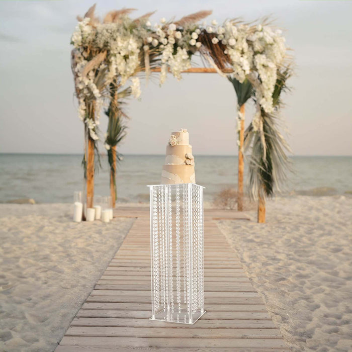Elegant wedding cake display under floral arch on beach.