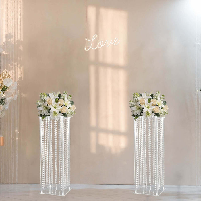 Elegant floral display on crystal pedestals with "Love" sign backdrop.