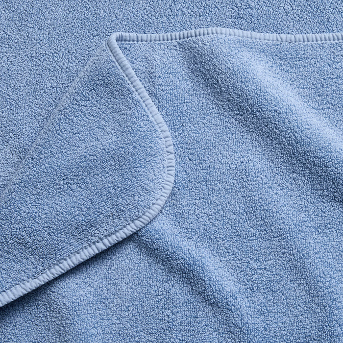 Close-up of a plush denim blue cotton bath sheet with a folded corner and finished stitched hem.