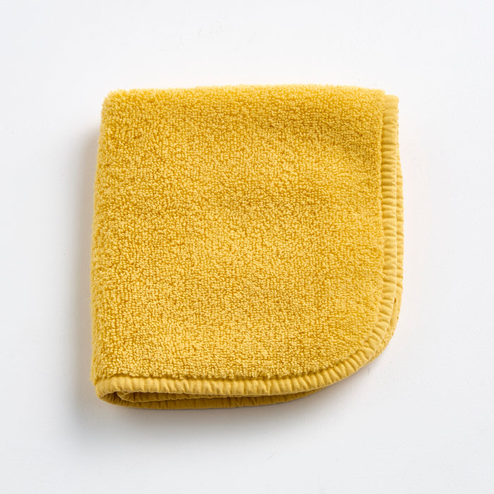 Folded yellow cotton terry washcloth with a stitched border on a white background.