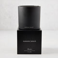 Hudson Grace Bleecker Scented 3-Wick Candle in a matte black glass vessel on its matching black gift box.