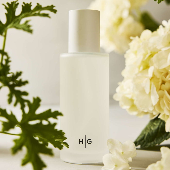 Hudson Grace Montauk 4oz frosted glass diffuser oil refill bottle with HG logo, surrounded by green leaves and white flowers.