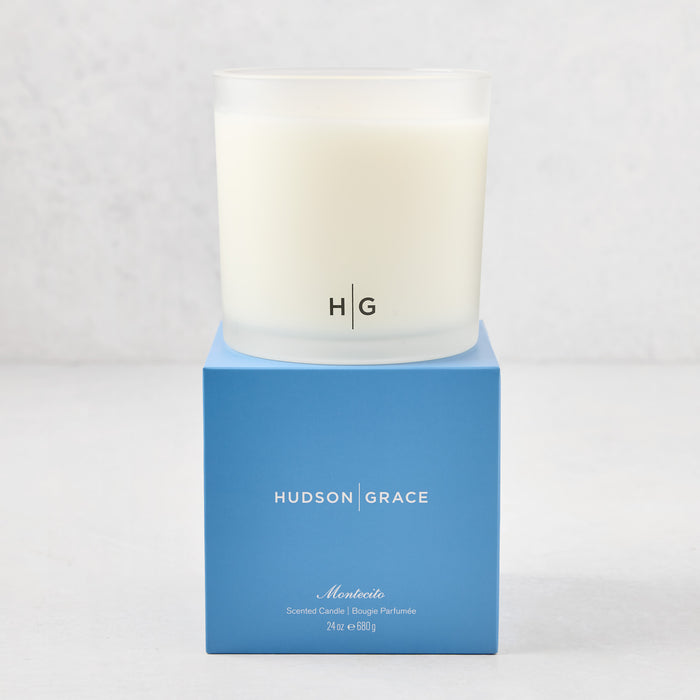 Hudson Grace Montecito 3-wick candle in a frosted glass vessel with HG logo, on a blue gift box.