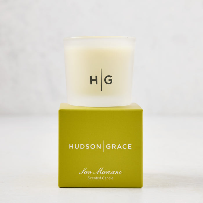 Hudson Grace San Marzano Votive Candle in a frosted glass vessel with HG logo, atop a green box.