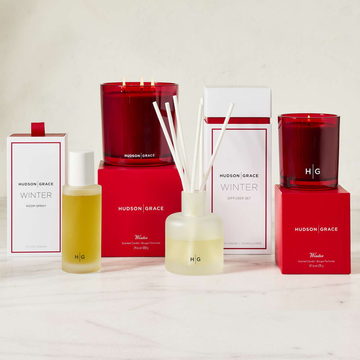 Hudson Grace Winter collection: red candles, room spray, and reed diffuser with white reeds and light yellow oil.