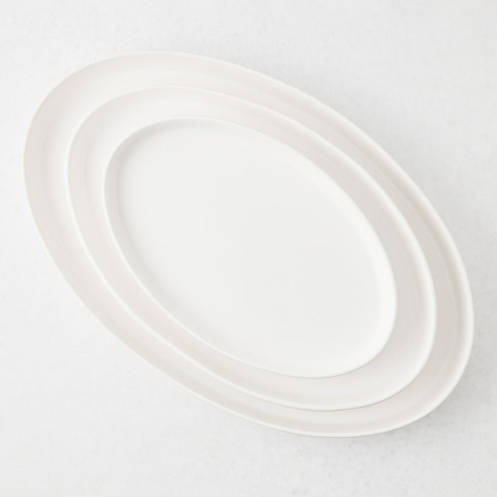 Three nested white stoneware oval serving platters on a light background.