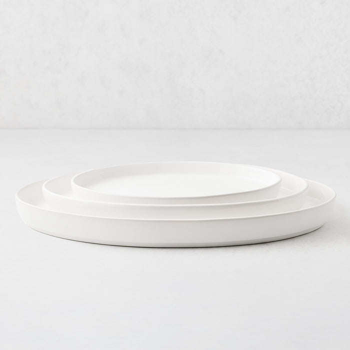 Three white oval stoneware nesting platters stacked on a light surface.