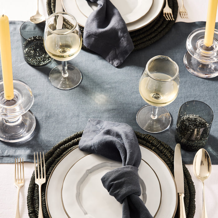 Clear glass taper candleholder with wide base and ridged design, holding a yellow candle on a set table.