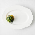 Large white ceramic Lungarno oval serving platter with scalloped edges and a small acorn squash.