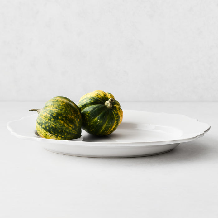 Large white ceramic Lungarno serve platter with soft scalloped edges holding two small green and yellow acorn squash.