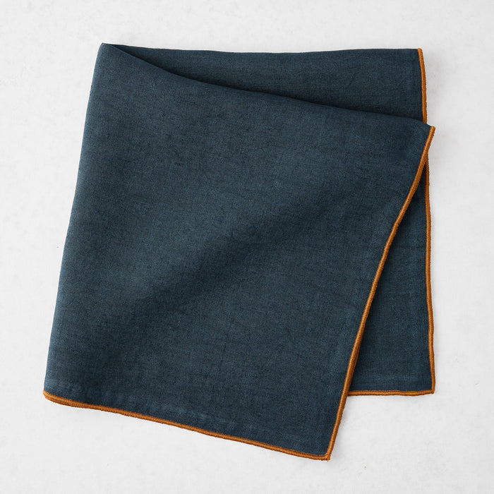 22-inch square navy blue linen napkin with a contrasting camel brown embroidered tipped stitch edge.