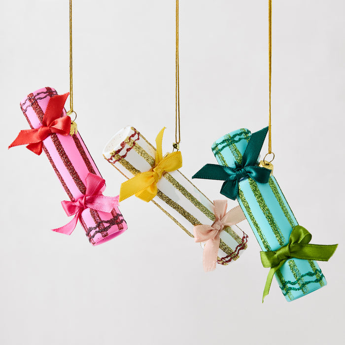 Three hanging Christmas cracker ornaments in pink, white, and teal, featuring glittered stripes and satin ribbon bows.