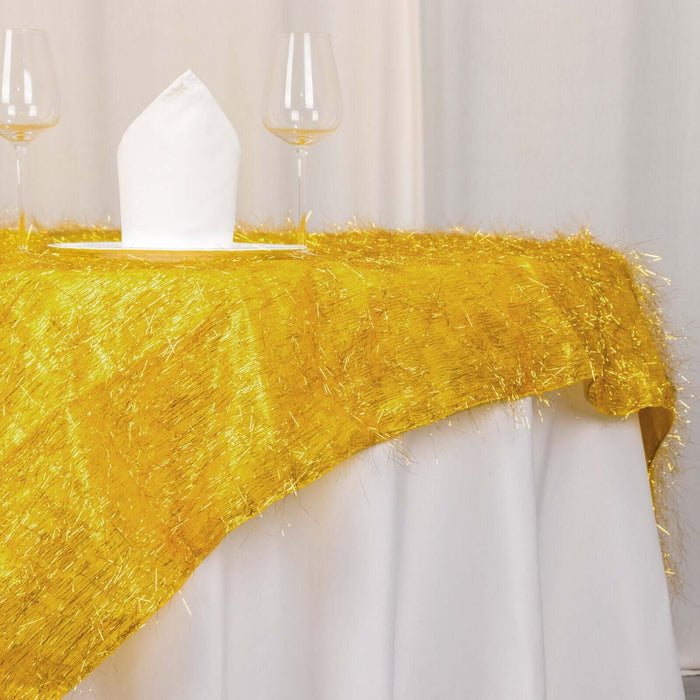 Gold fringed table runner on a white tablecloth with glasses and a napkin.