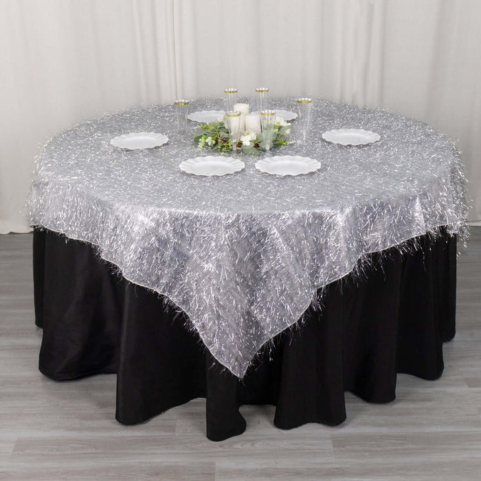 Round silver tablecloth with fringe on a black table, elegantly set for dining.