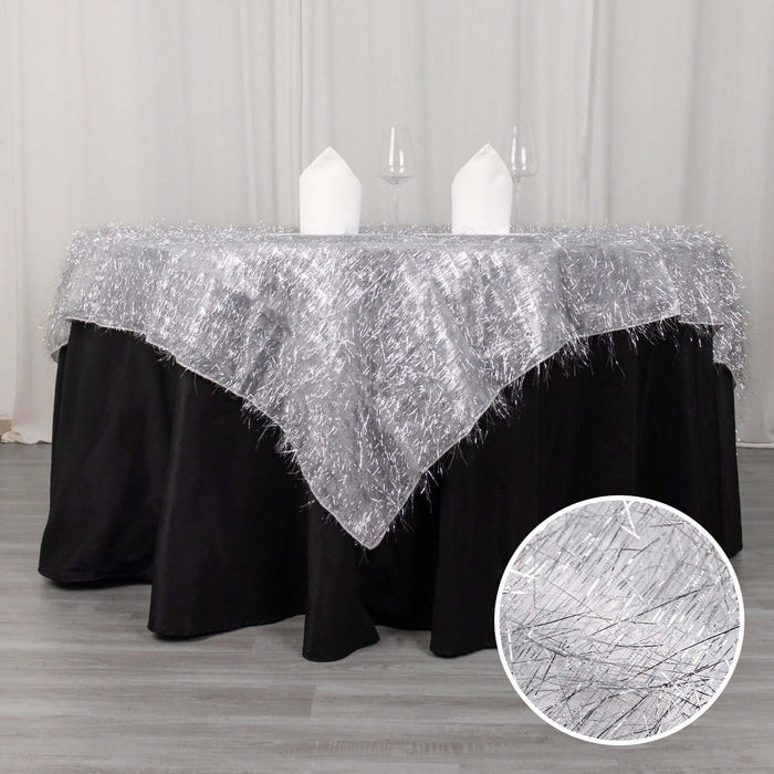 Silver fringed tablecloth on a black table with white napkins and wine glasses.