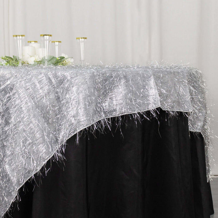 Silver table overlay on a black tablecloth with candles and greenery.