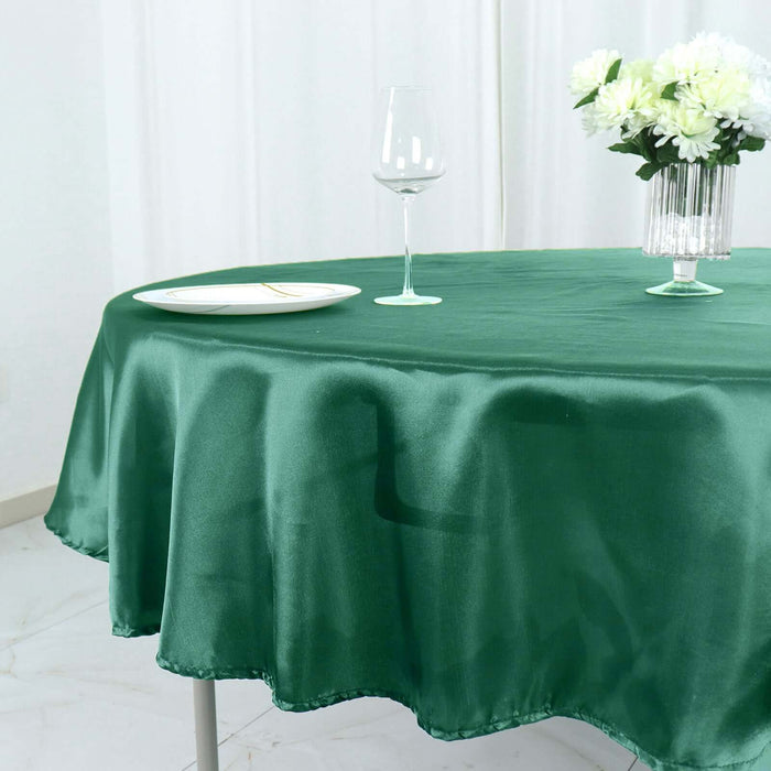 Green round tablecloth draping over a table with a glass and flowers