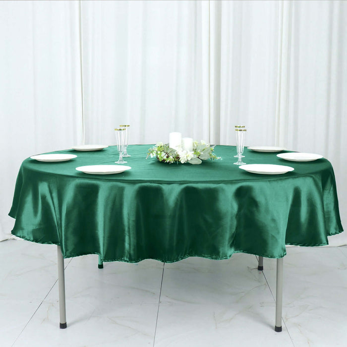 Round green satin tablecloth on a dining table set with plates and candles.