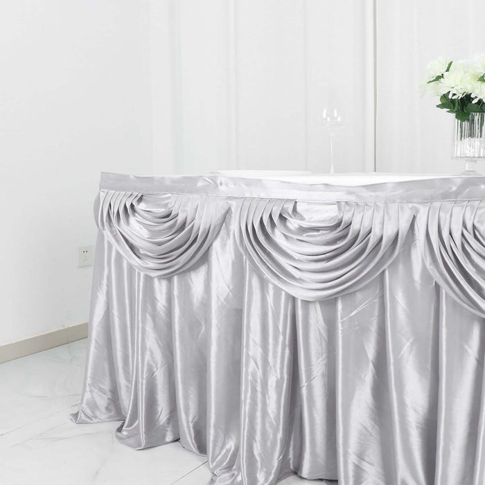 Silver satin table skirt with elegant draping for event decor.