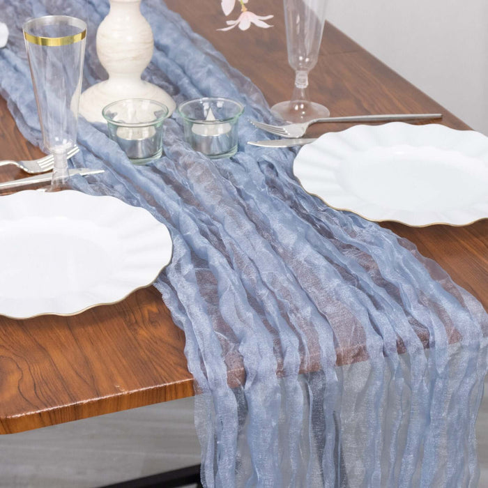 Light blue sheer table runner draped on a wooden dining table with elegant tableware.