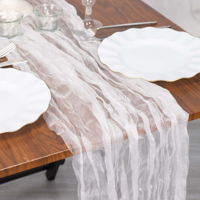 Sheer white table runner on a wooden dining table with plates and glassware.