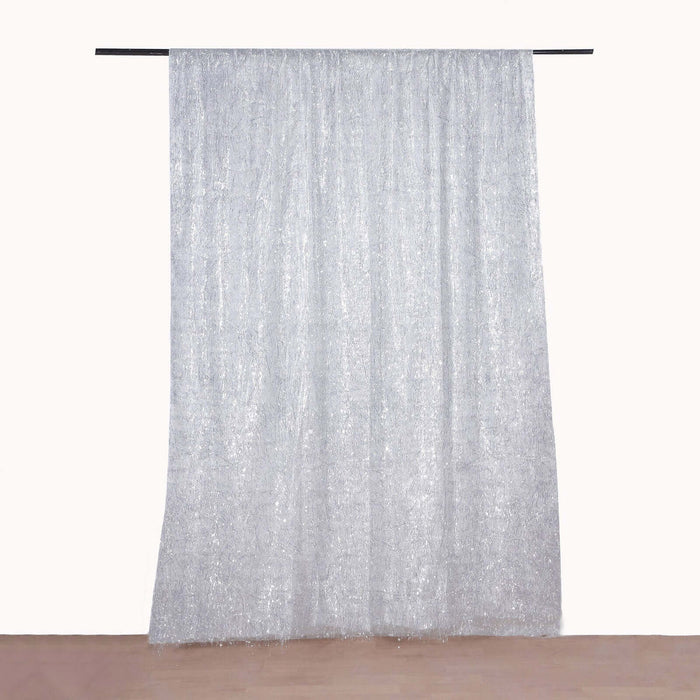 Sheer silver curtain hanging from a rod on a plain backdrop.