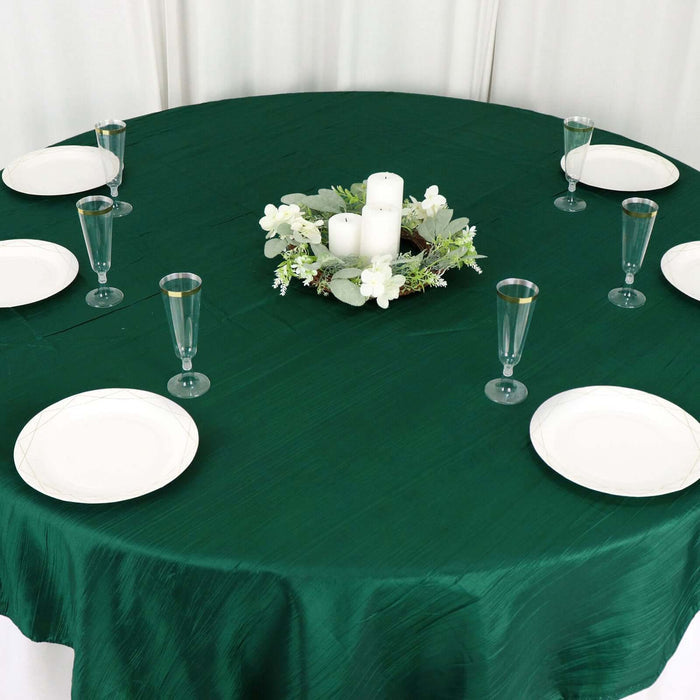 Green tablecloth with white plates and a floral centerpiece on a round table.
