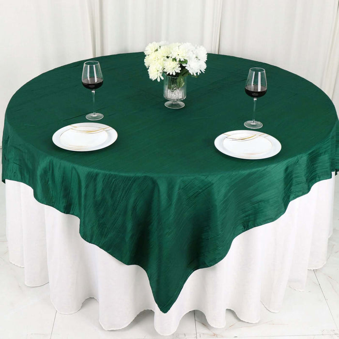 Green round tablecloth on a dining table set with plates and wine glasses.