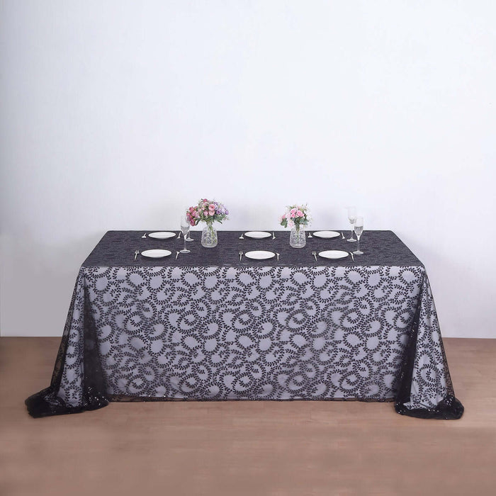 Black lace tablecloth on a dining table set with plates and floral centerpieces.