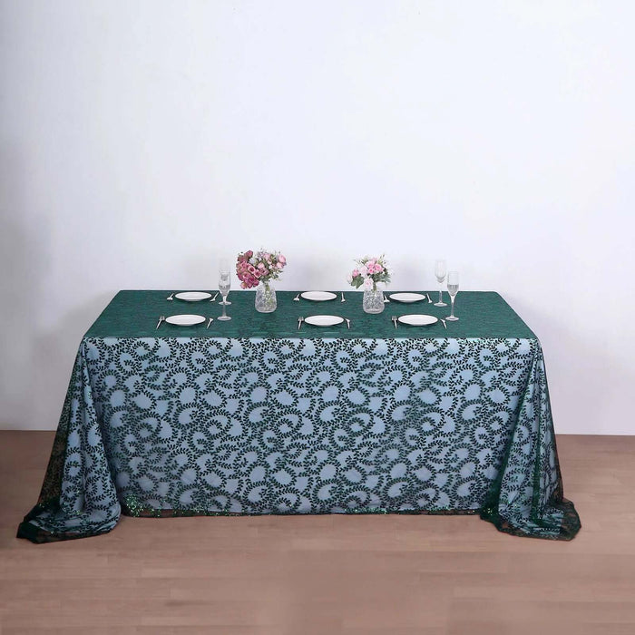 Elegant green tablecloth with floral design, set for dining with plates and flowers.