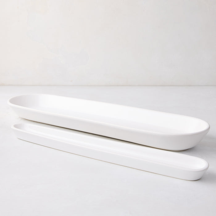 Two white ceramic olive serving trays, one large and one small, with an oval shape.